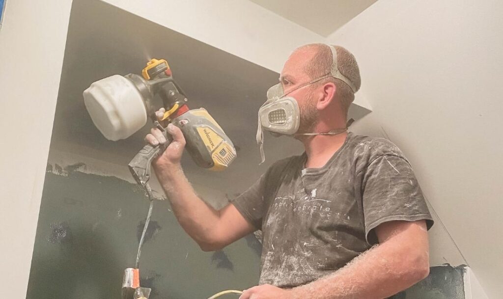 man painting ceiling in a bathroom with a flexio paint sprayer