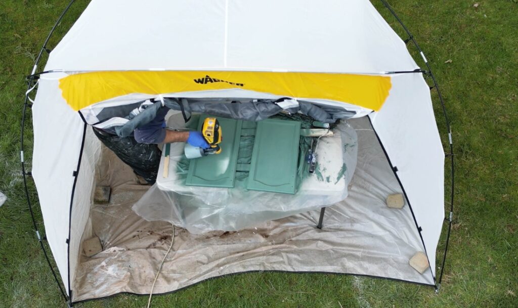 person spraying cabinets inside spray tent with paint sprayer