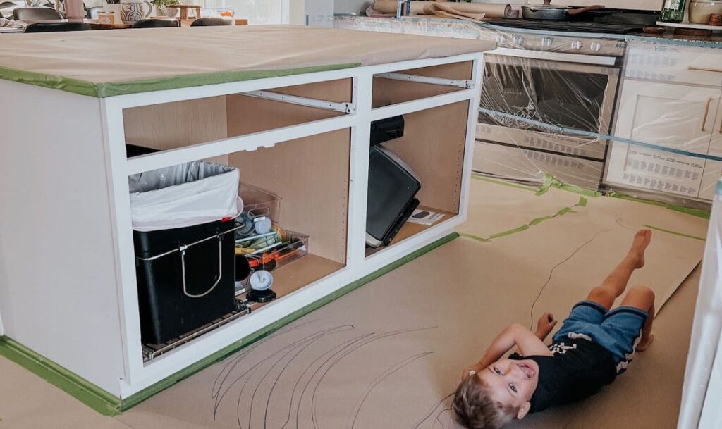 prep work for painting, child laying down in front of kitchen island