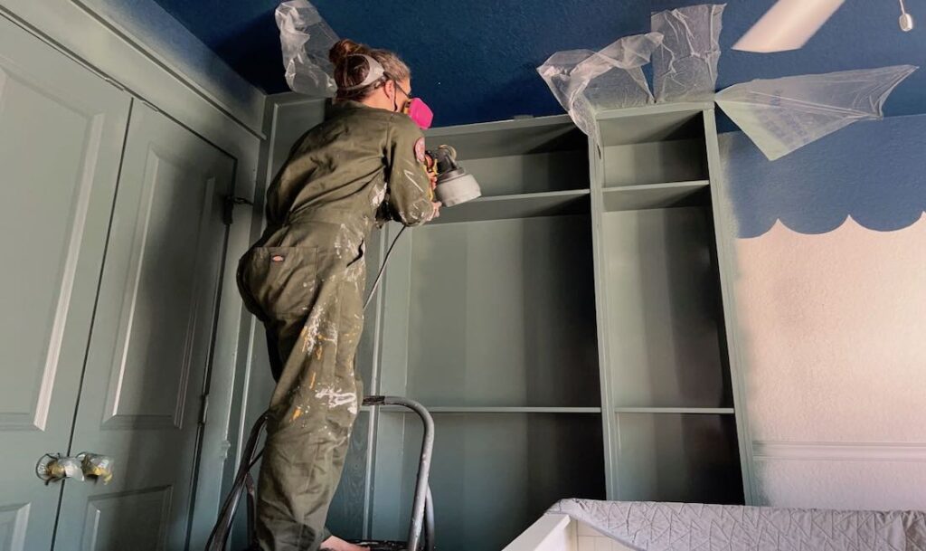woman painting built in shelves that she installed in the bedroom. Army green paint and outfit