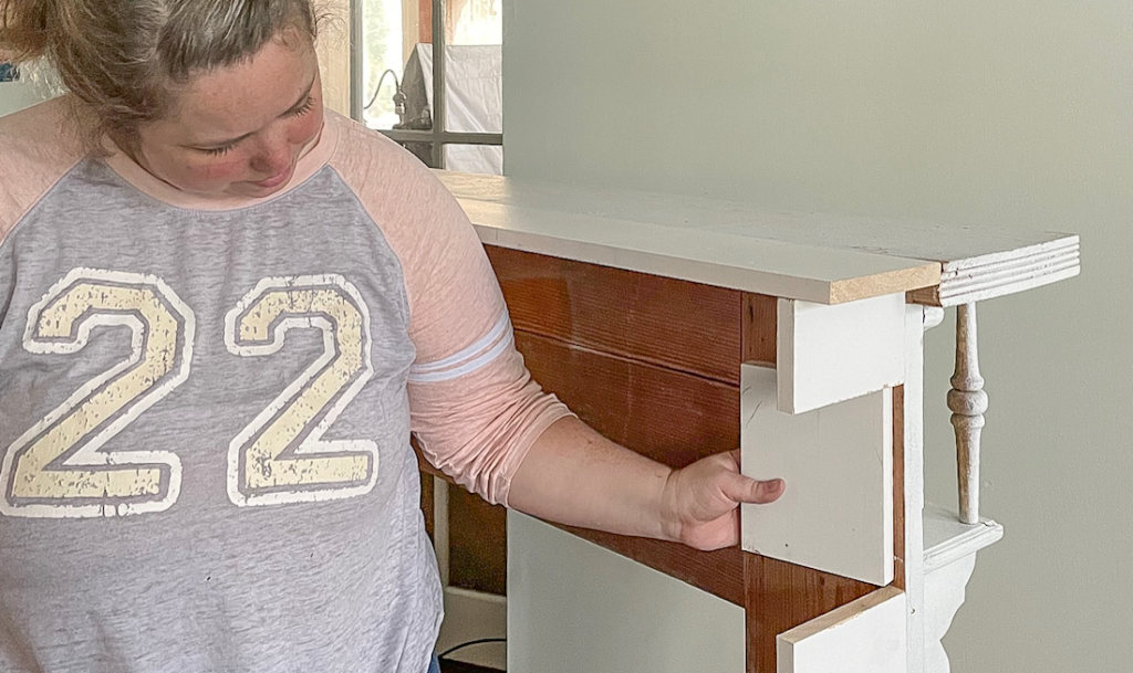 person holding a block of wood to add the hinge door to the mantle