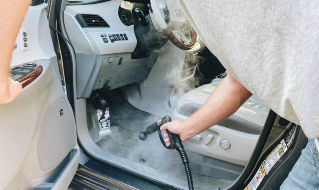 up close shot of man steam cleaning the carpet in his car