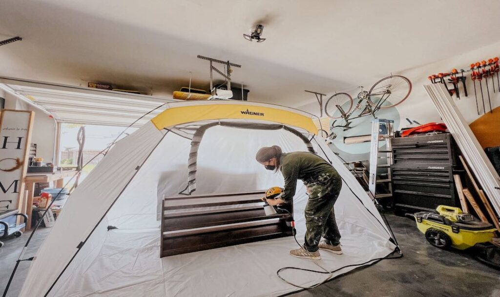 person spraying furniture inside of a Wagner large spray tent inside of a garage