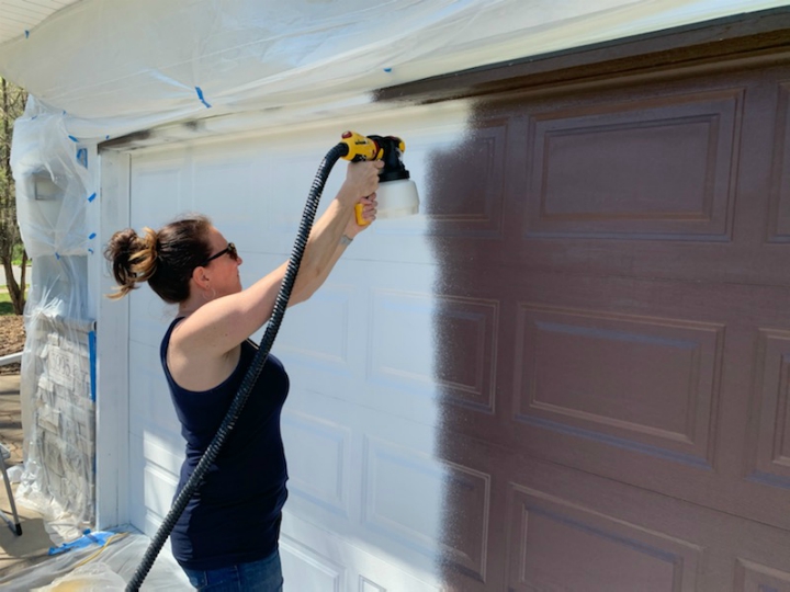 woman spraying a garage door with a paint sprayer