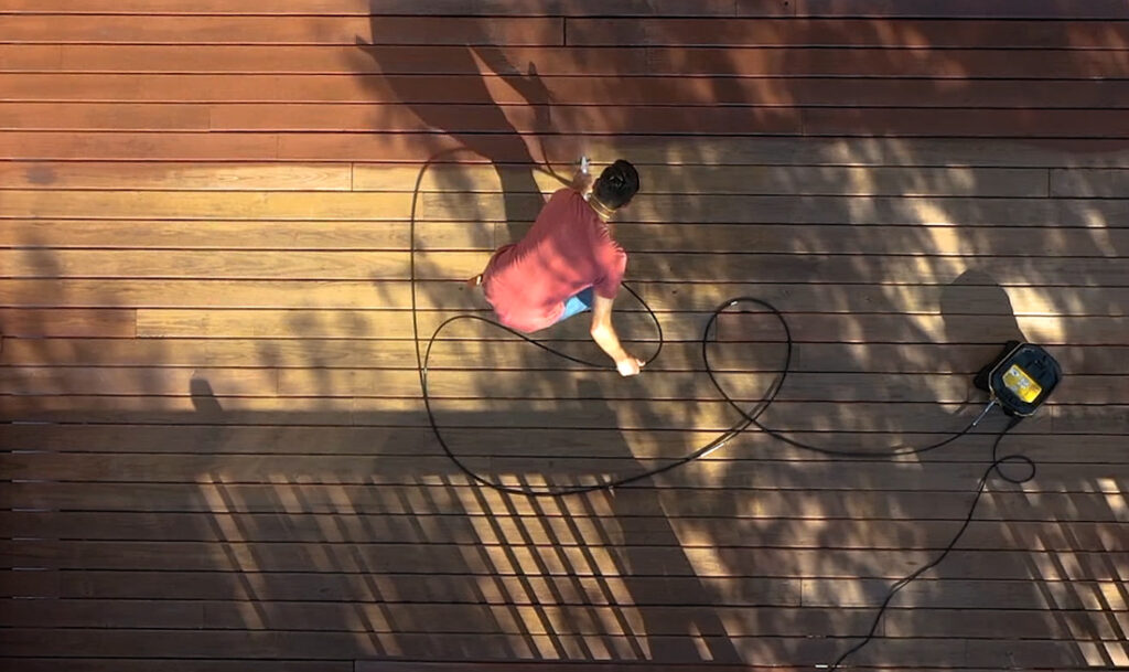 man in red shirt spraying deck boards with stain