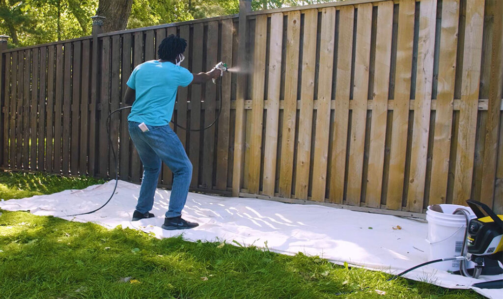 staining fence with wagner sprayer on the ground