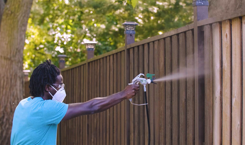 spraying stain on wooden fence 